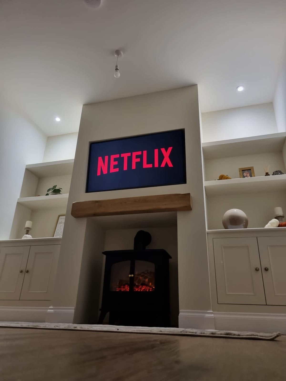 Fitted alcove cupboards and shelving flanking a log burner with a wall-mounted TV