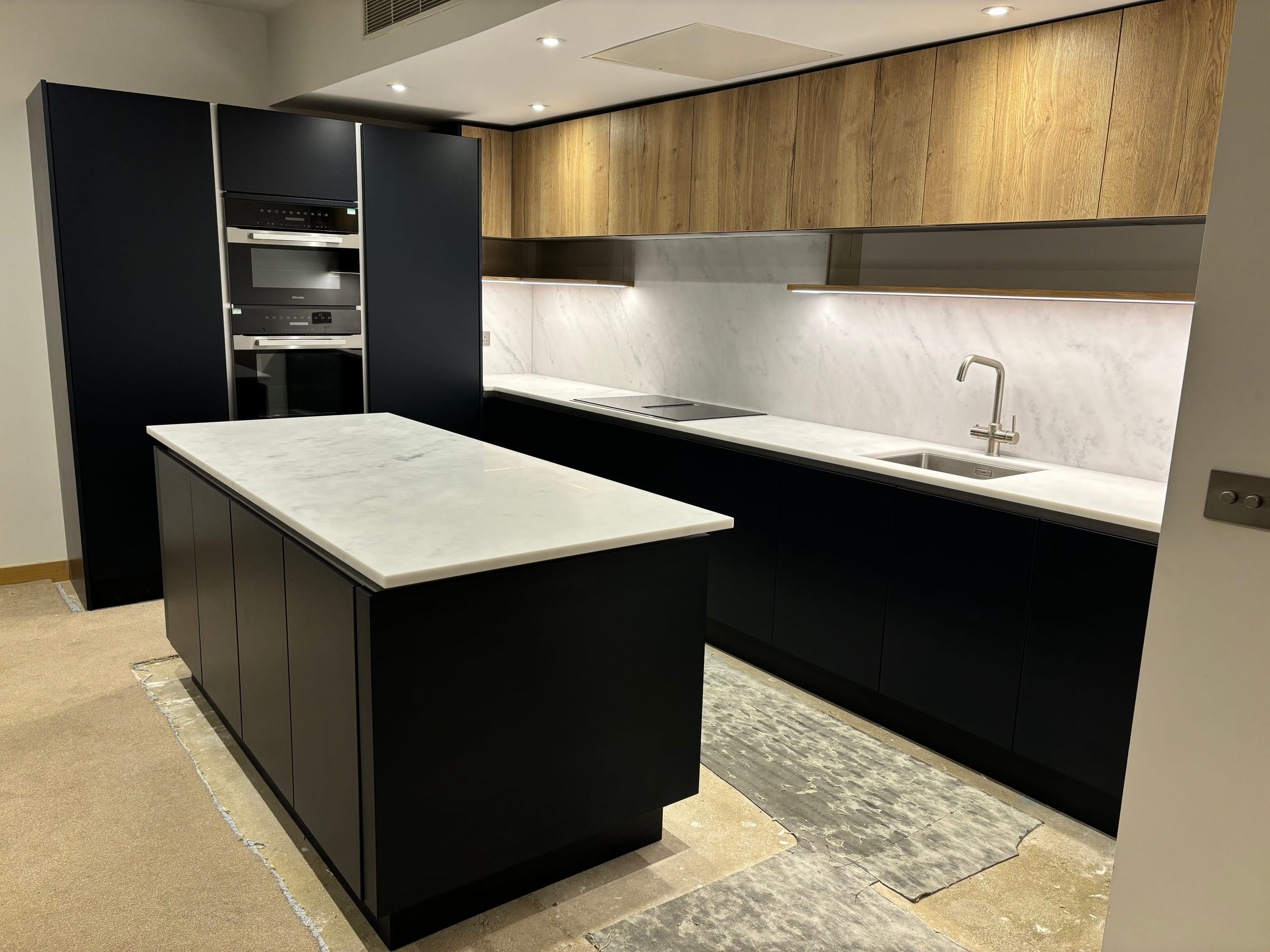 Contemporary black kitchen with a marble-topped island, oak wall units and integrated ovens