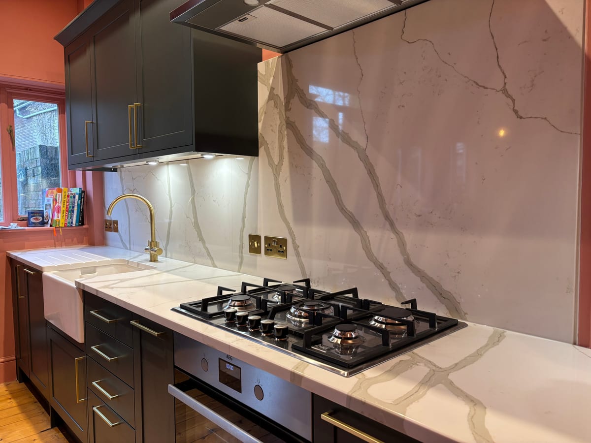 Bespoke kitchen with a veined marble splashback, gas hob and brass mixer tap