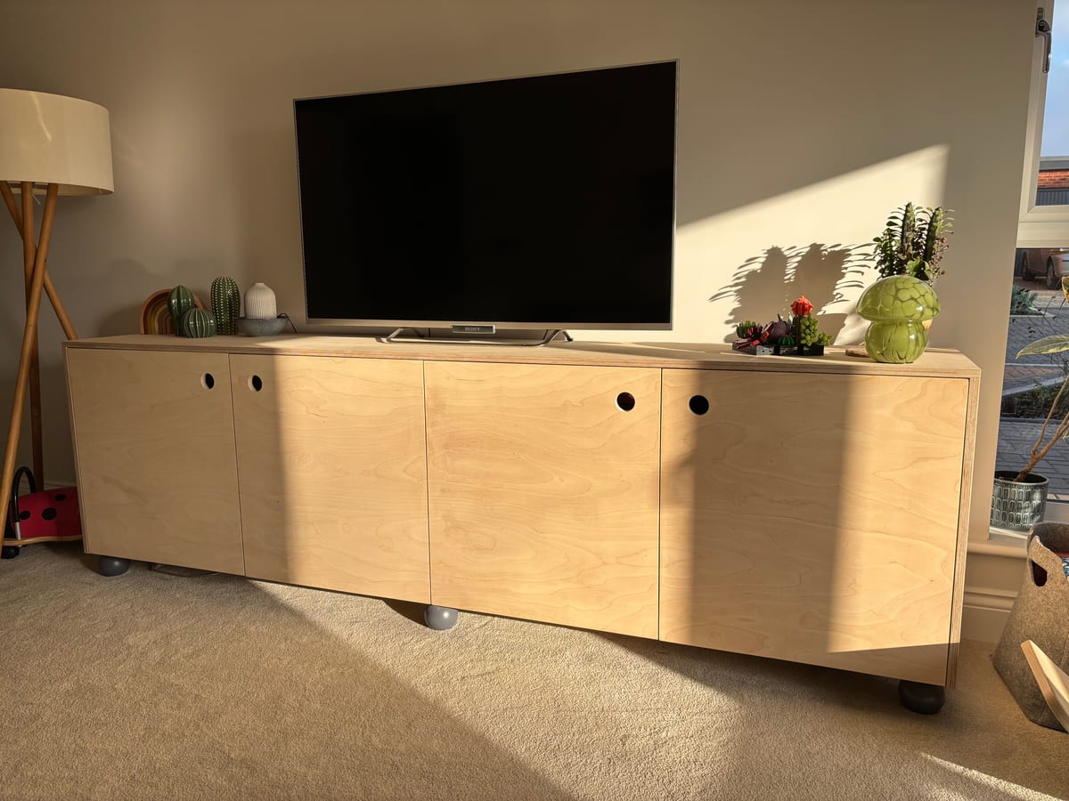 Birch plywood media unit on castors with sliding doors beneath a wall-mounted TV