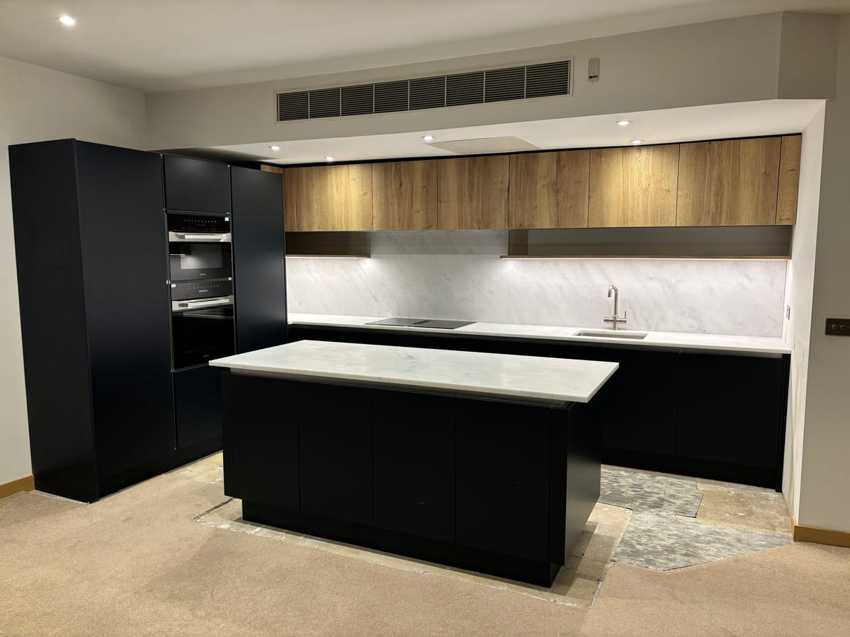 Black handleless kitchen with a large island, oak wall units and marble splashback