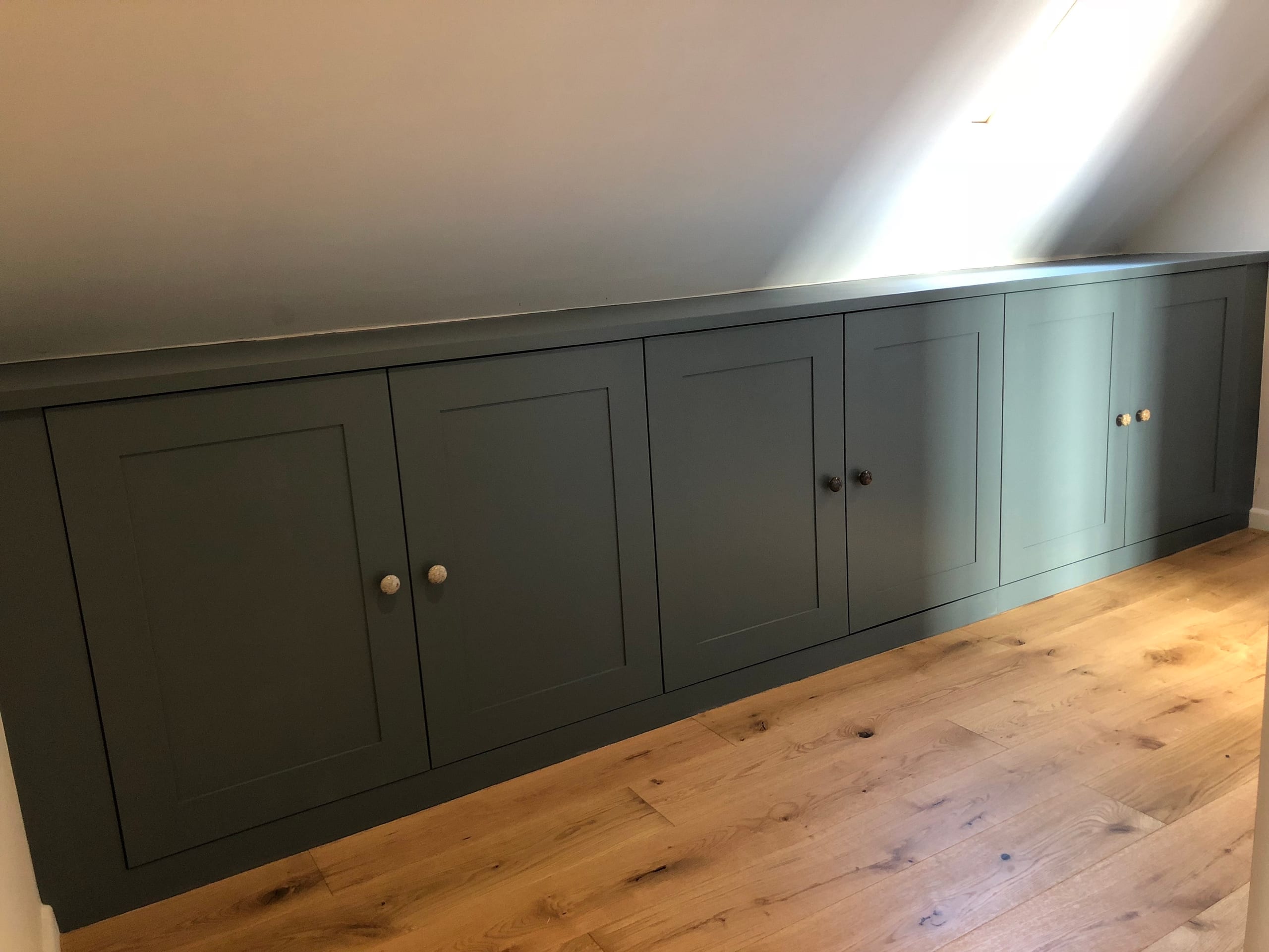 Long run of bespoke fitted cupboards painted deep green above a solid oak floor
