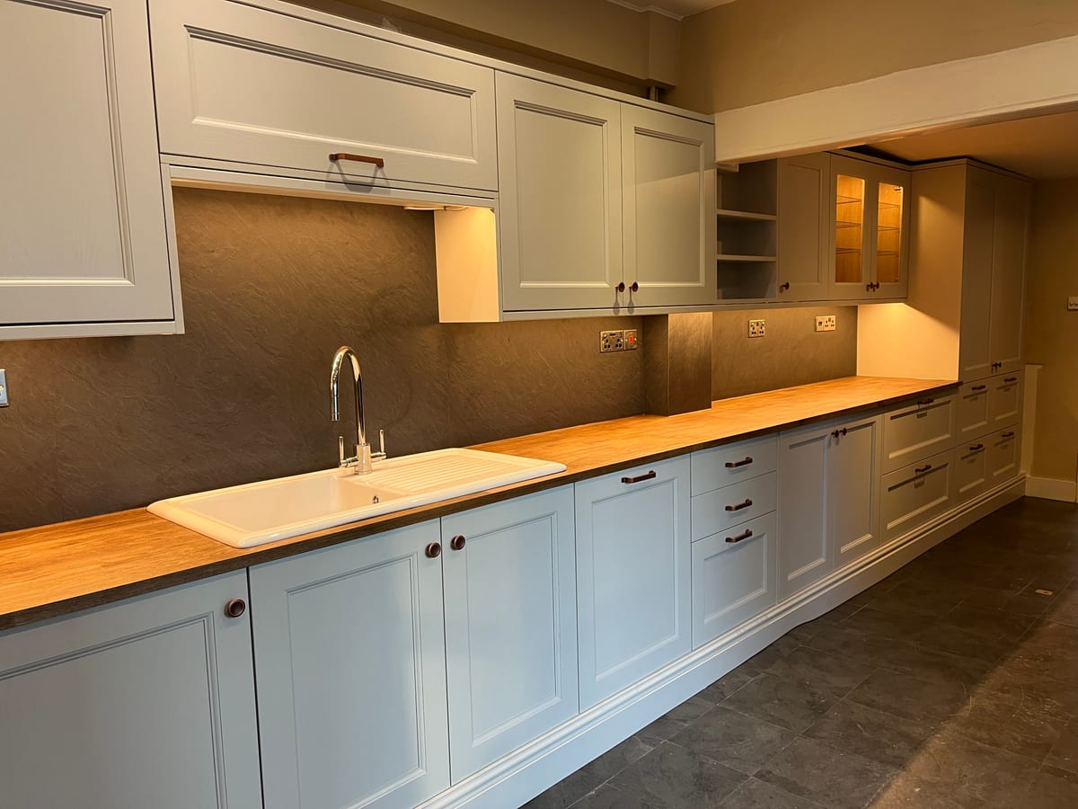 Long run of cream kitchen cabinetry with an oak worktop and undermount sink