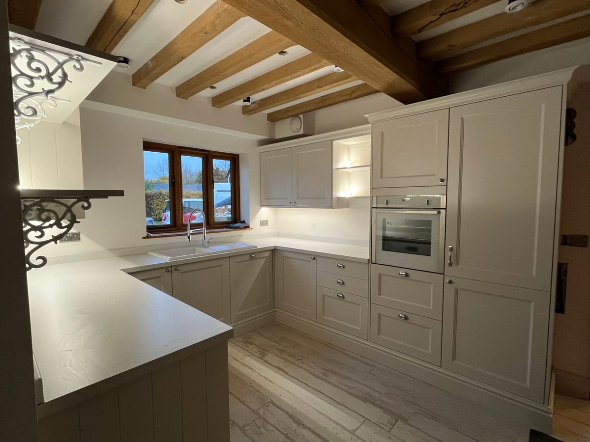 Cream shaker kitchen beneath exposed oak beams with a peninsula and double oven