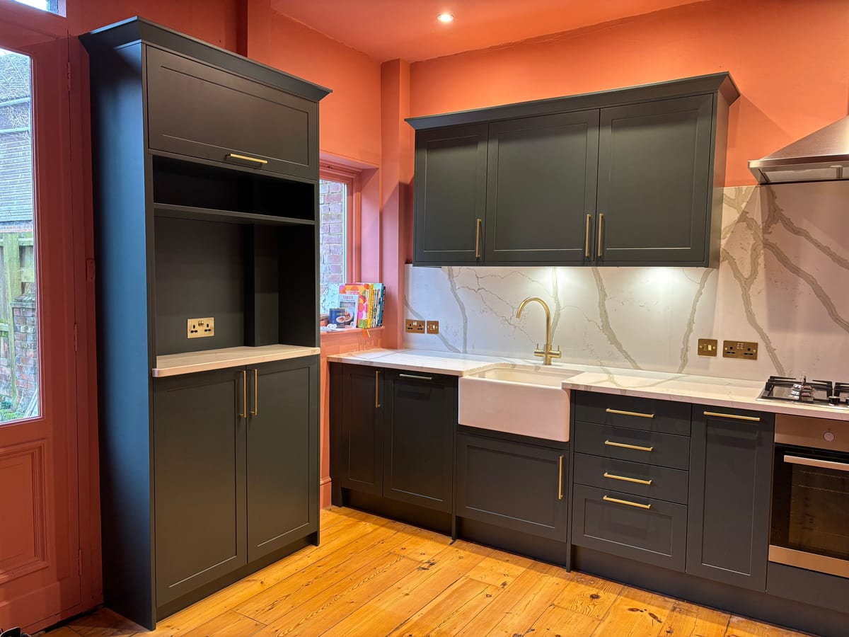 Dark green kitchen with tall larder units, marble splashback and brass handles