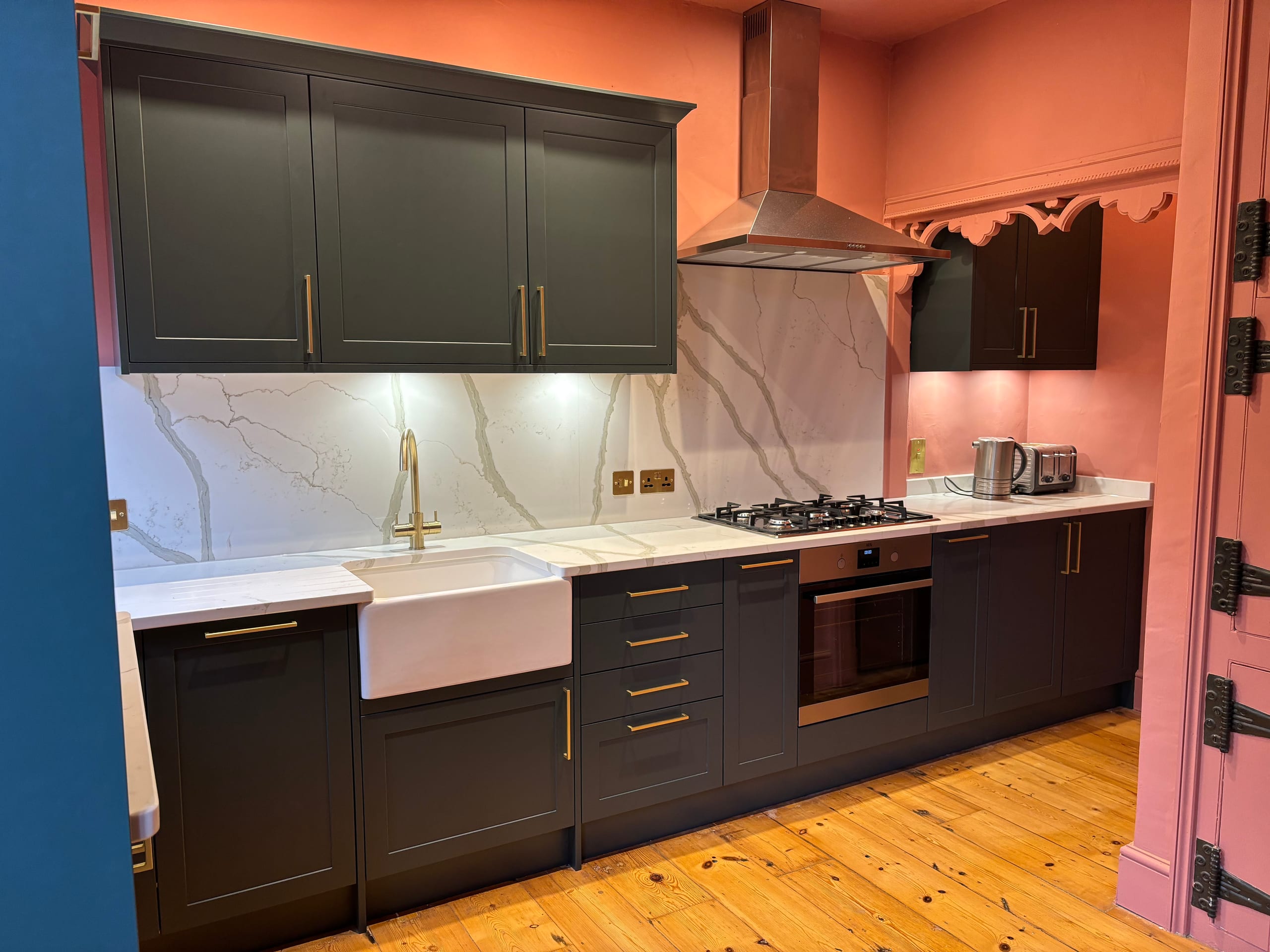 Dark green shaker kitchen with a marble splashback, brass handles and a butler sink