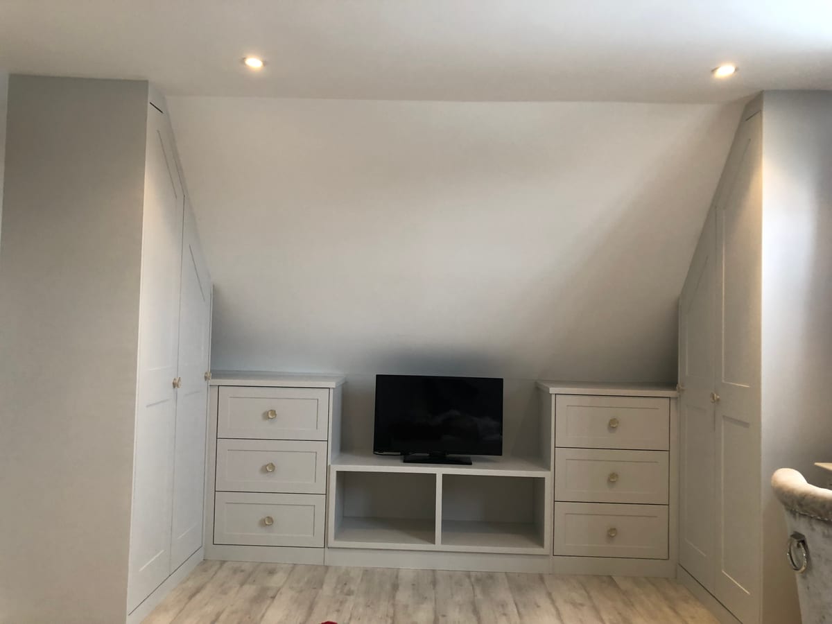 Fitted eaves drawers and a media shelf built into a sloping bedroom wall