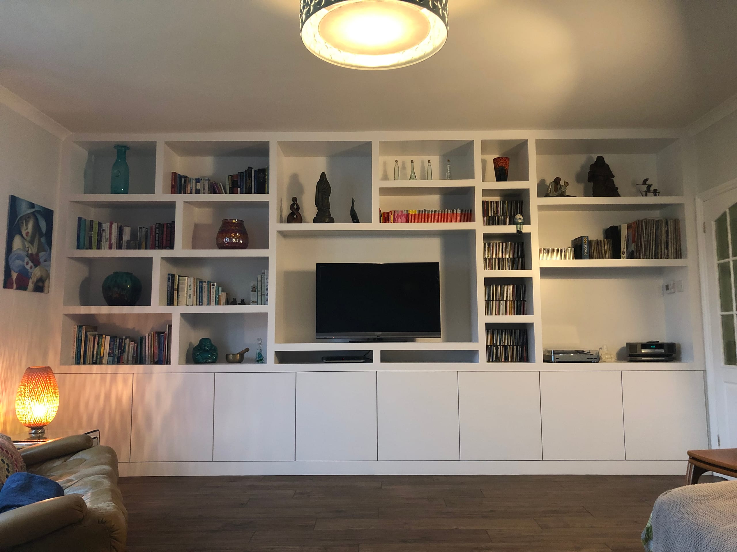 Floor-to-ceiling fitted bookcase and media wall spanning a living room, painted white