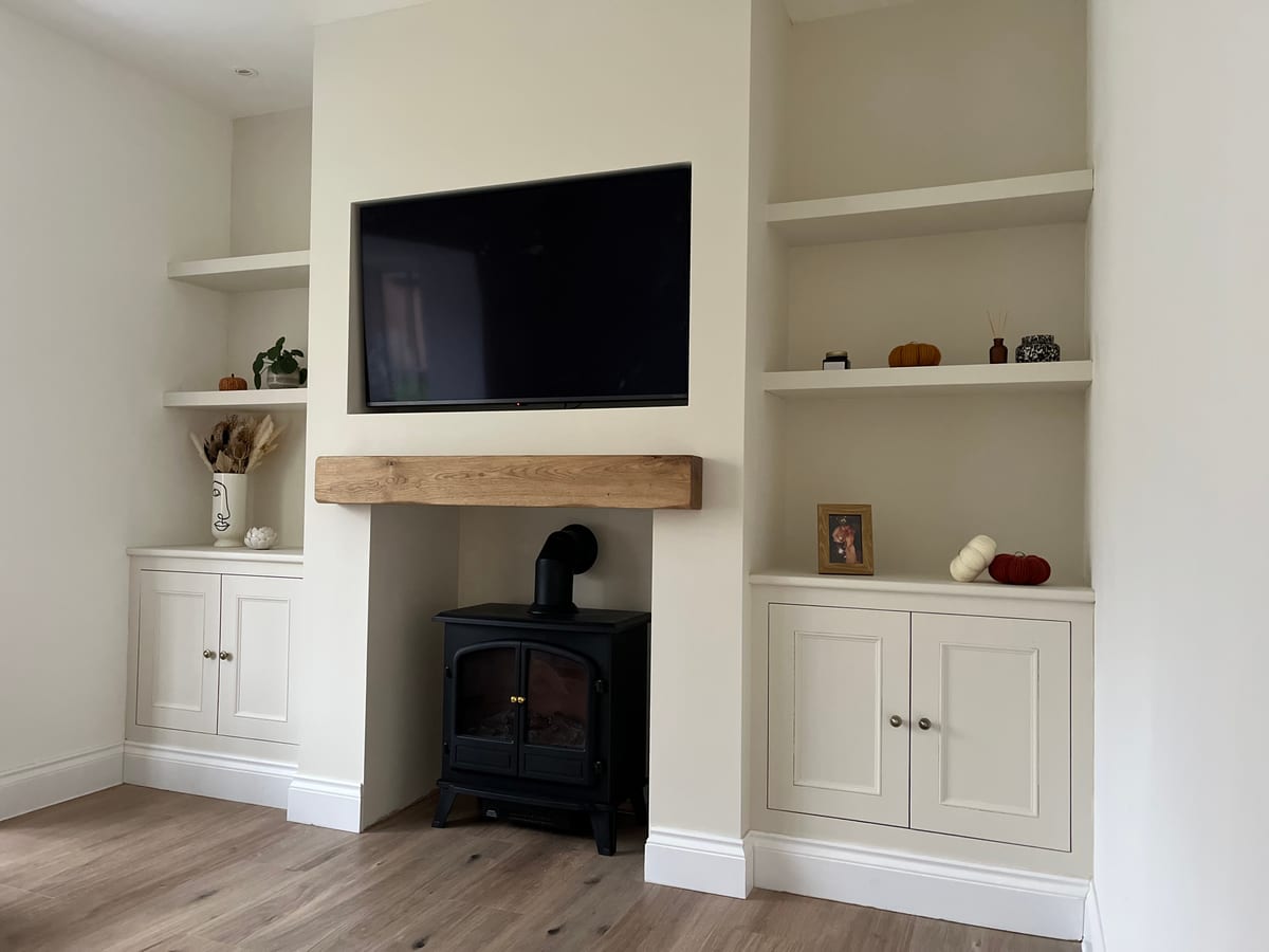 Fitted alcove cupboards and shelving either side of a log burner with an oak mantel