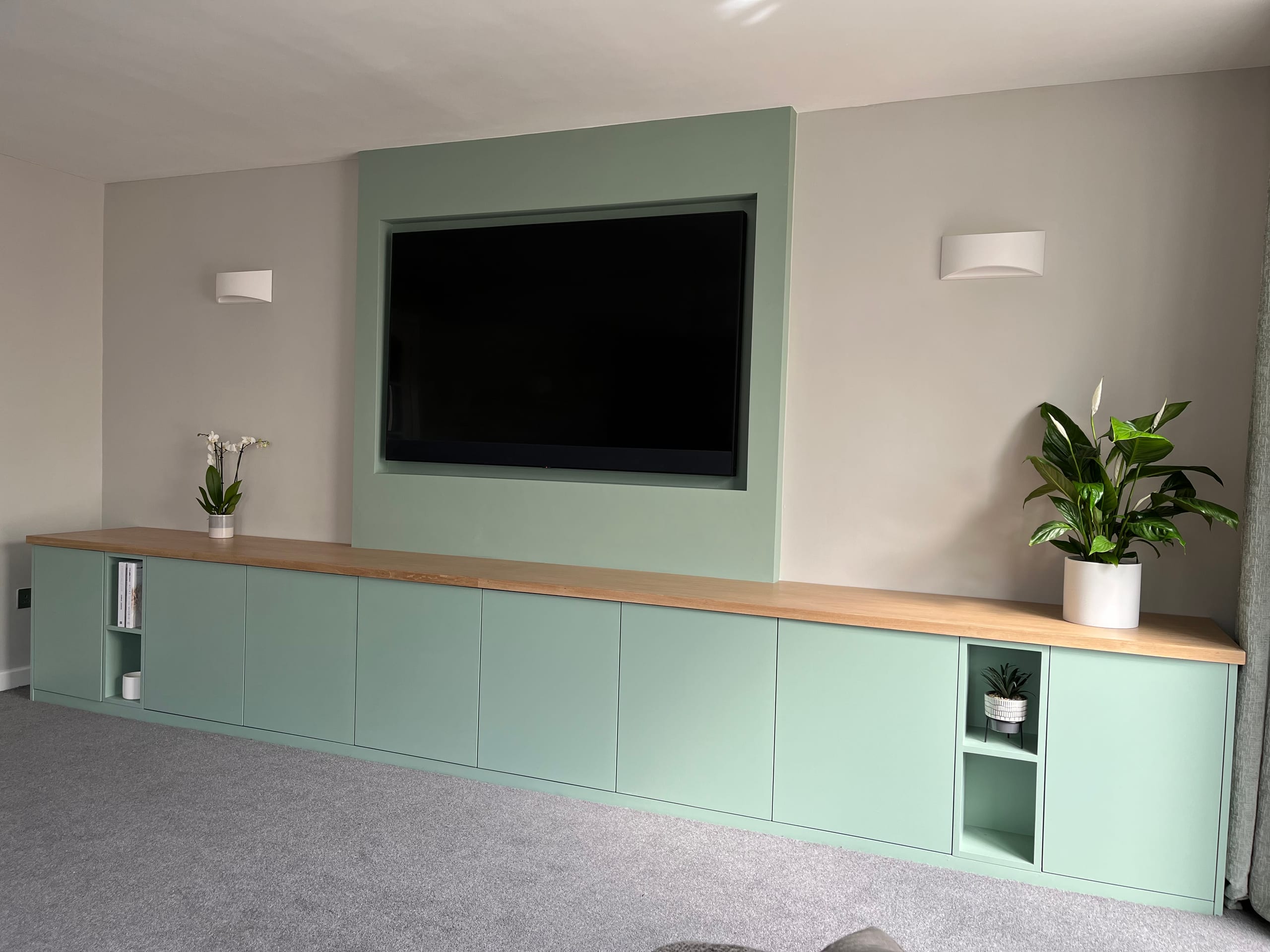 Full-width fitted sideboard and media unit in sage green with a solid oak top