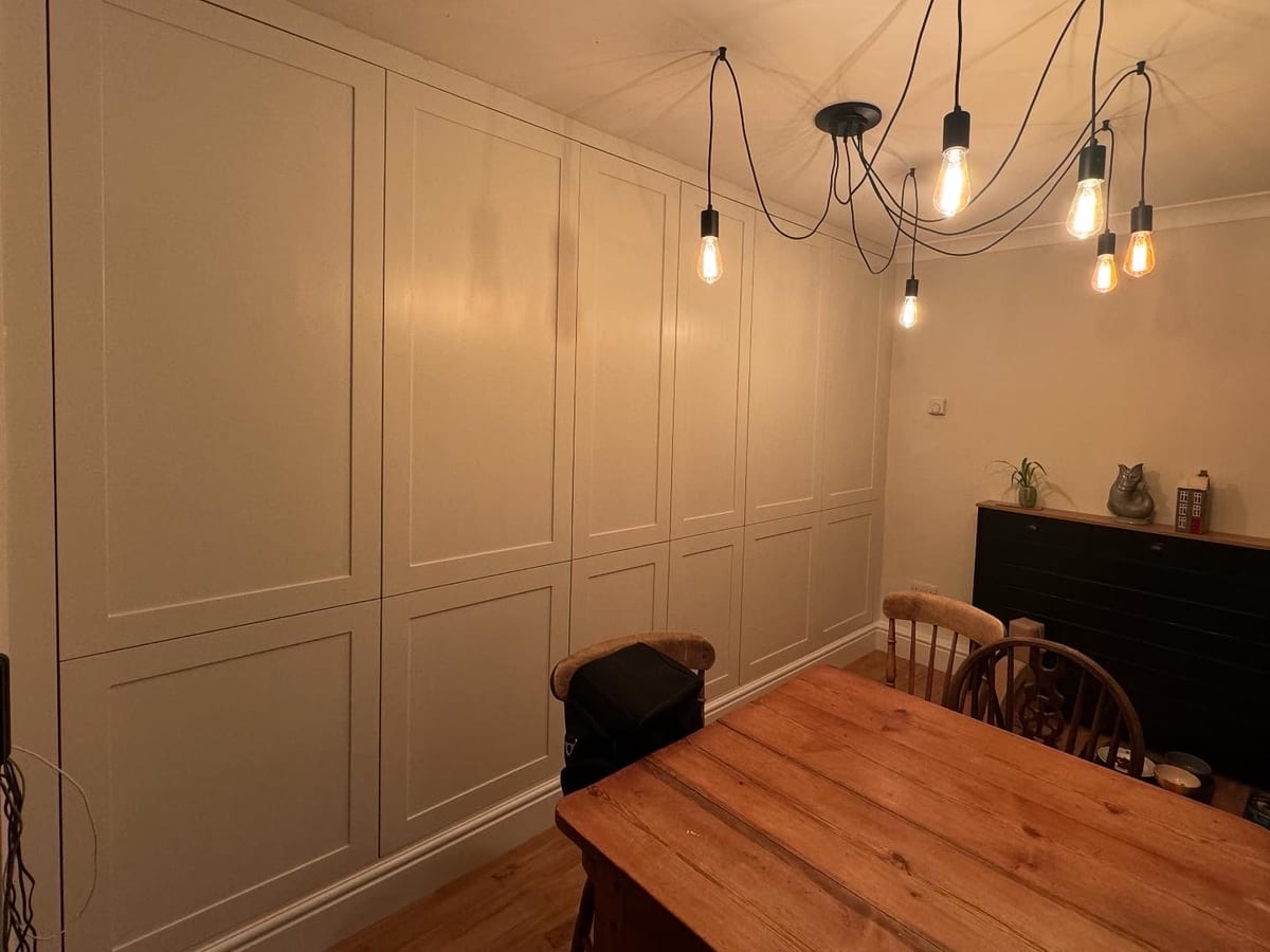 Wall of fitted wardrobes painted off-white in a dining room with pendant lighting