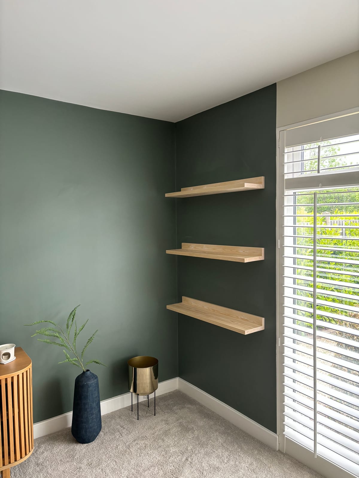 Oak floating shelves fitted into an alcove against a dark green wall