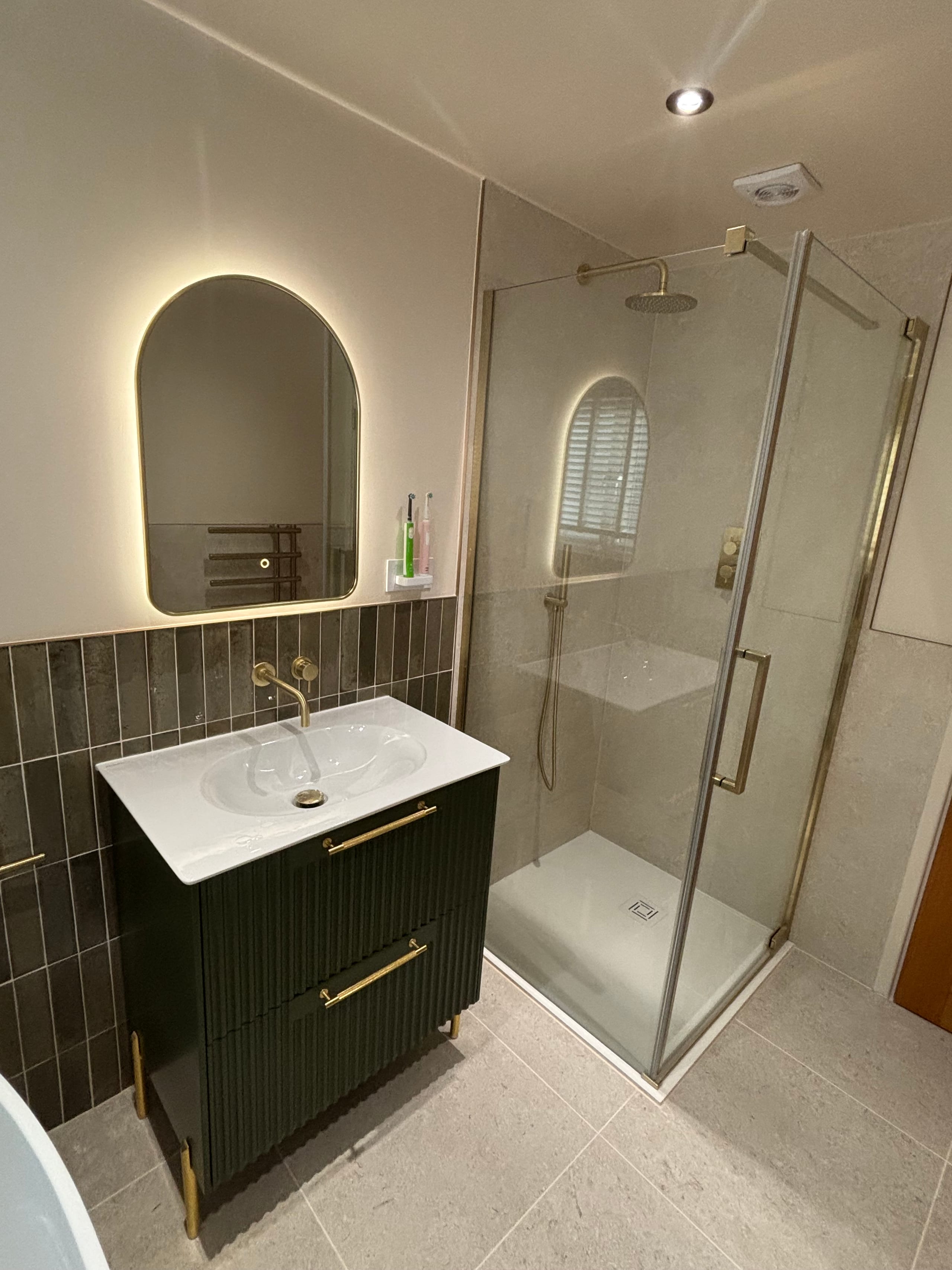 Bathroom with a green fluted vanity unit, arched backlit mirror and walk-in shower
