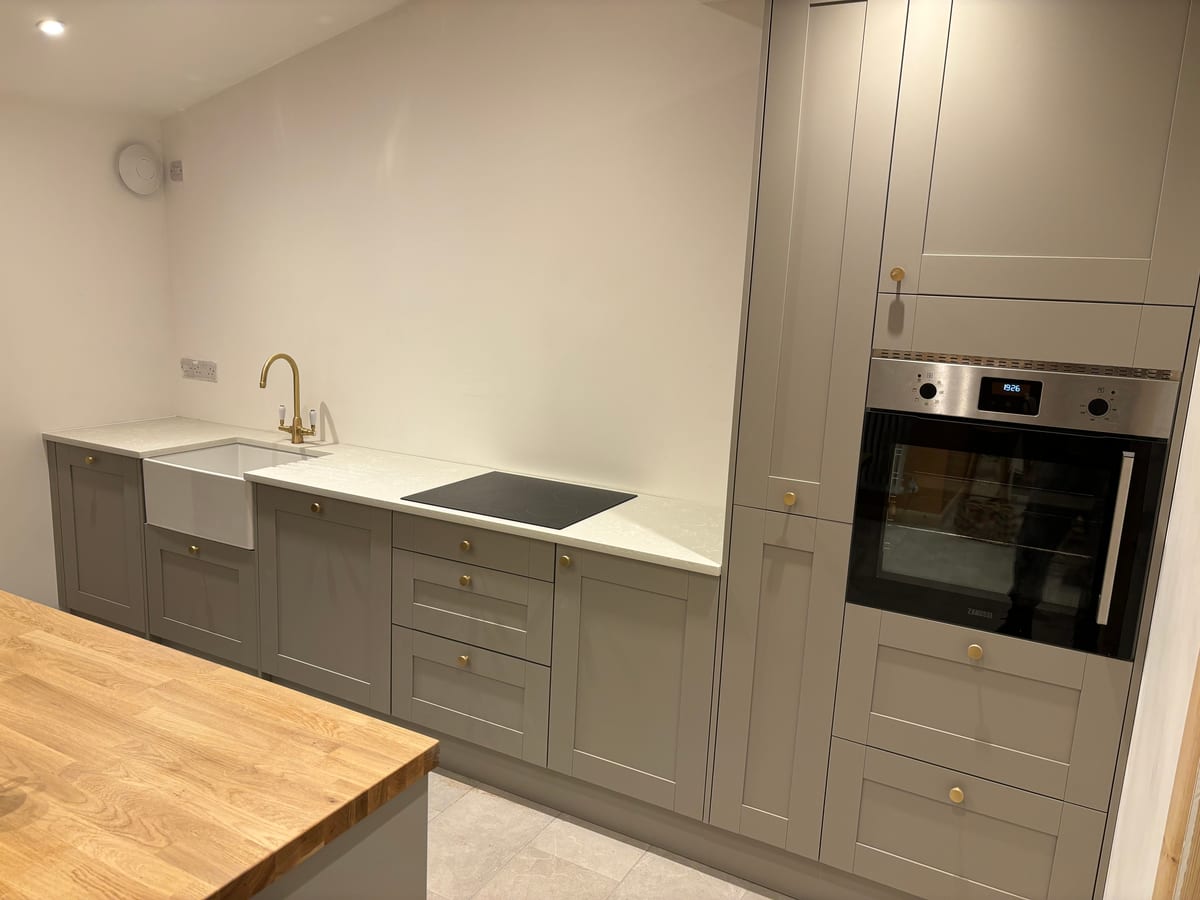 Grey kitchen with a Belfast sink, brass tap, oak worktop and built-in oven