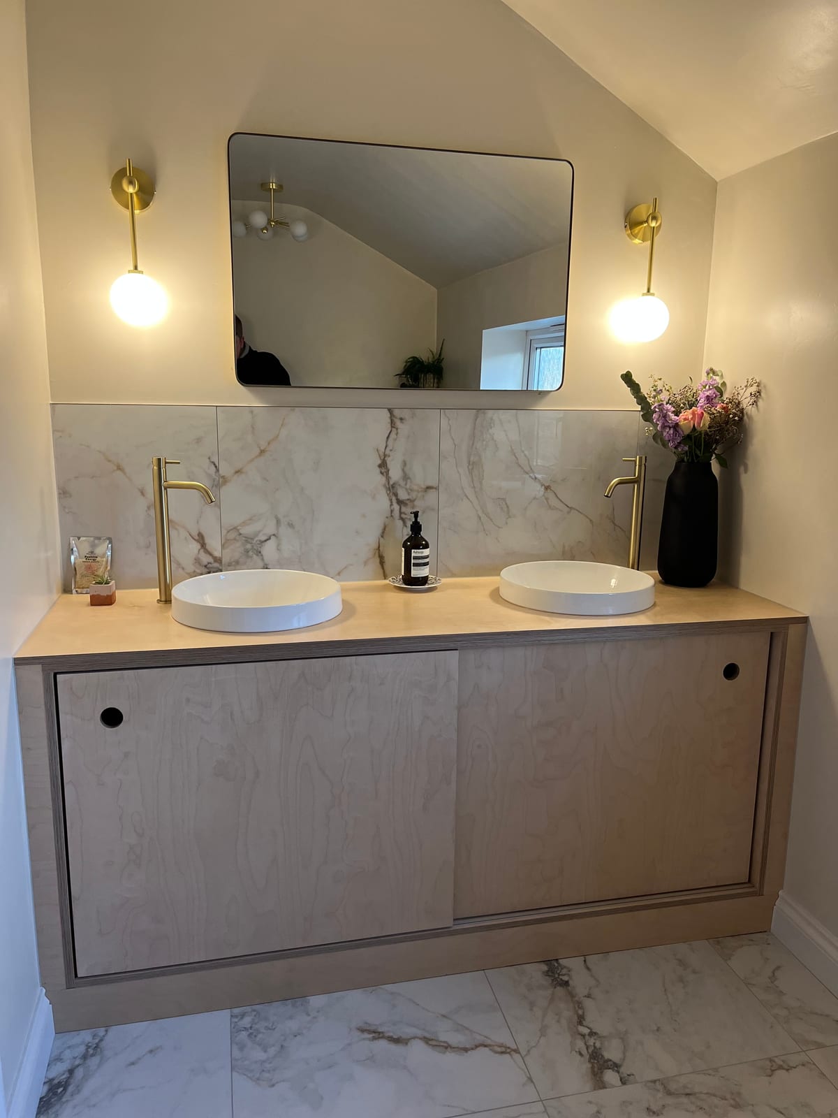 Handmade twin-basin vanity unit with a marble splashback and brass wall lights