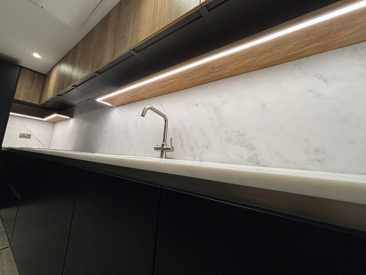 Close detail of a marble splashback with a lit oak shelf above dark cabinetry