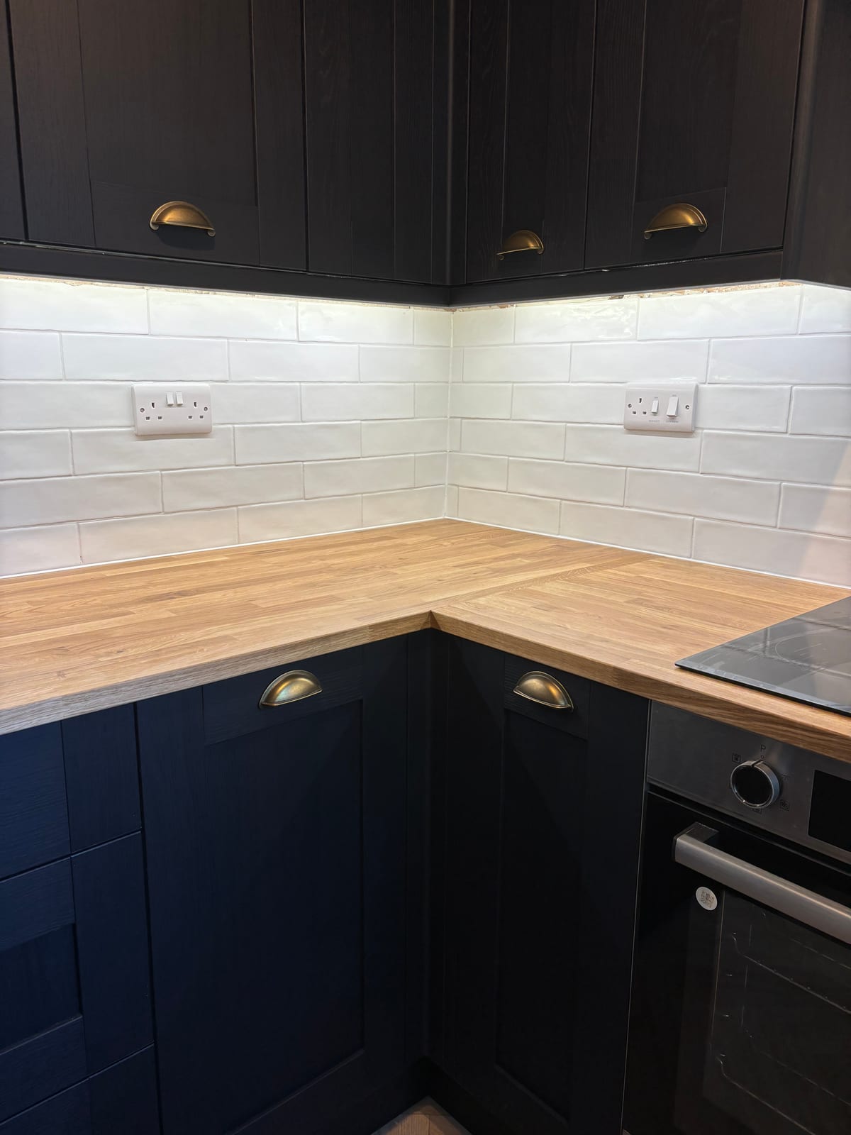 Navy blue kitchen units with a solid oak worktop and tiled splashback