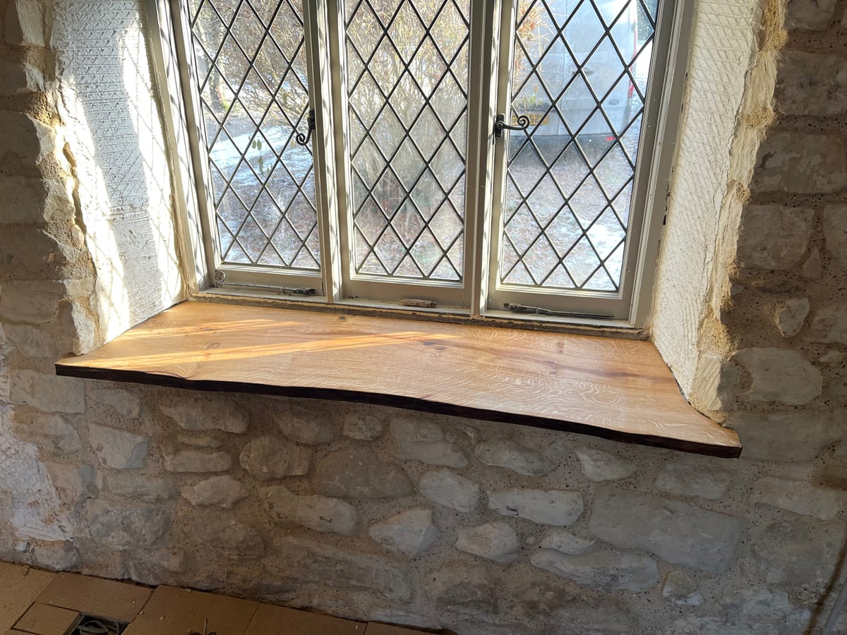 Solid oak window sill fitted into a stone wall beneath a leaded cottage window