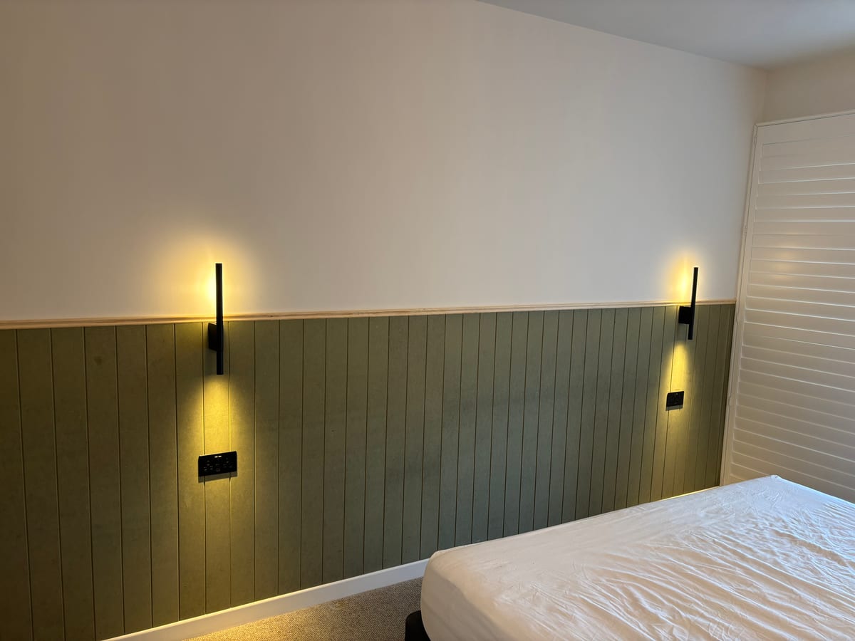 Green tongue-and-groove panelled headboard wall with fitted reading lights