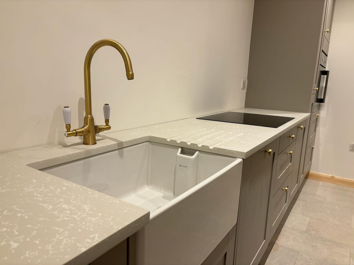 White quartz worktop with a butler sink, brass swan-neck tap and induction hob