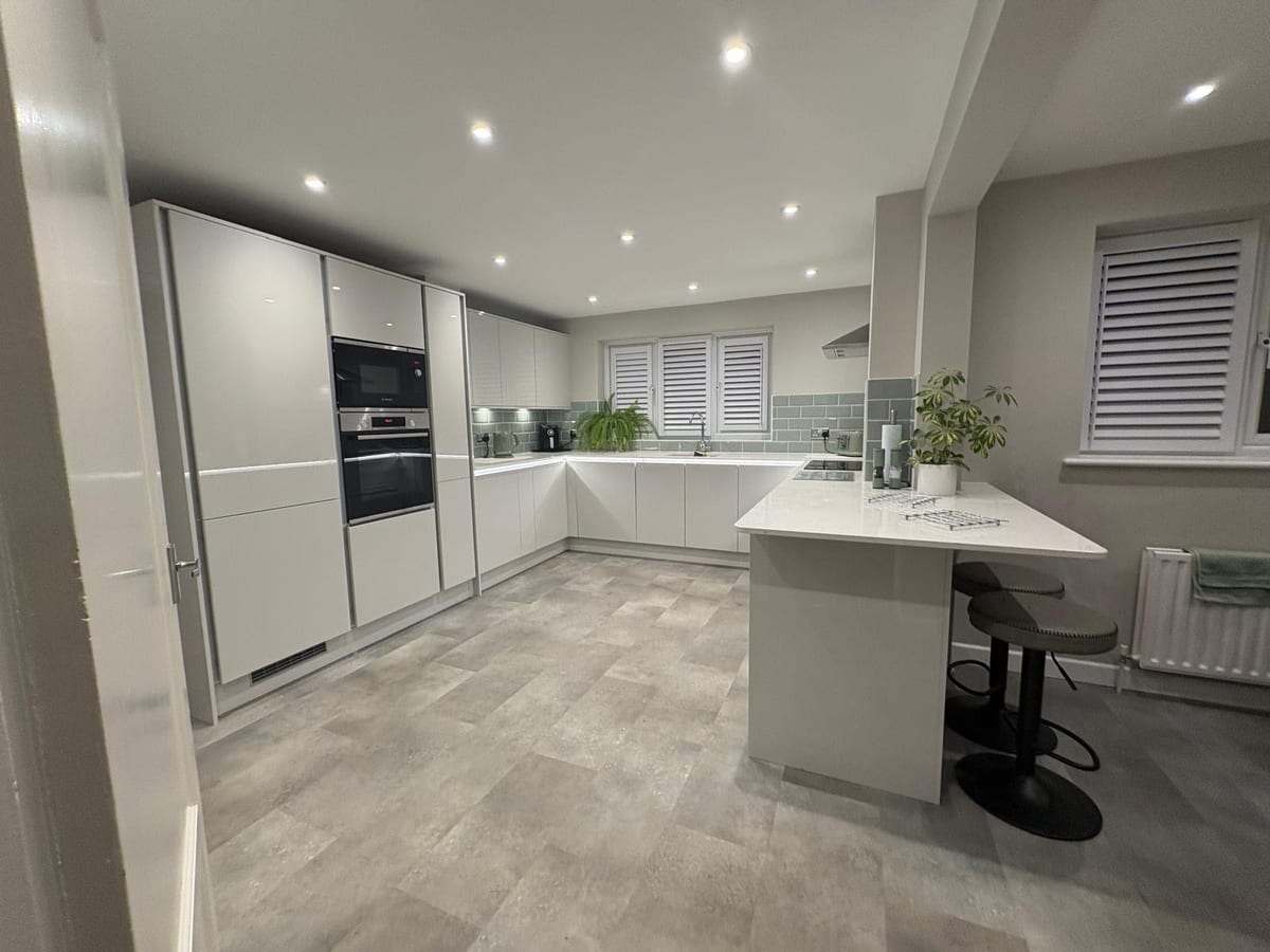 Bright white kitchen with an island breakfast bar, bar stools and tall units
